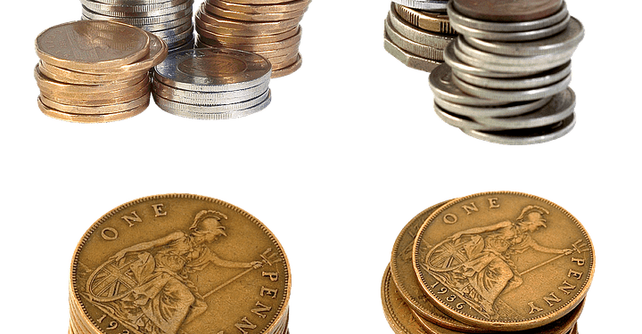 Stacks of various coins including British pennies in silver, copper, and bronze tones.