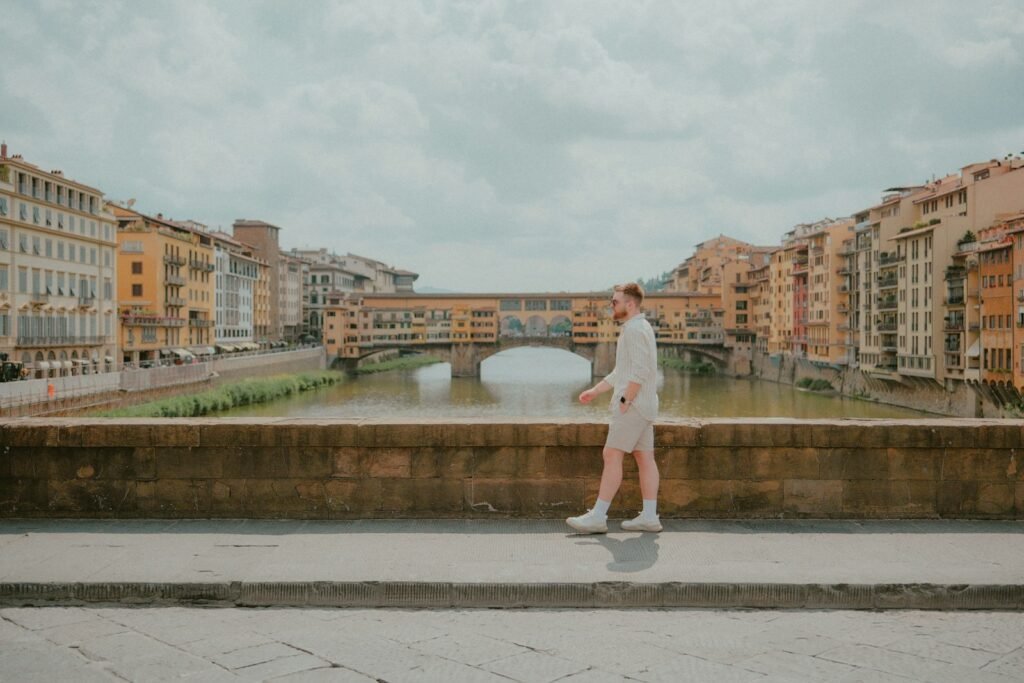 Man walks along a bridge, with buildings in the background.