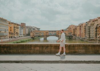 Man walks along a bridge, with buildings in the background.