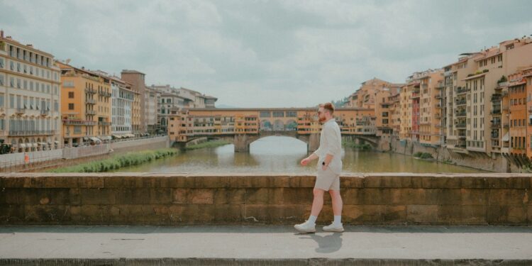 Man walks along a bridge, with buildings in the background.