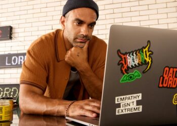 Man wearing a beanie and shirt works on a laptop.