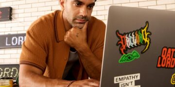 Man wearing a beanie and shirt works on a laptop.