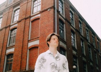 Young man stands before a brick building