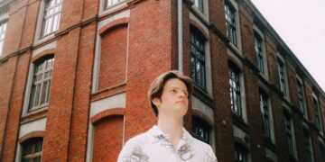 Young man stands before a brick building