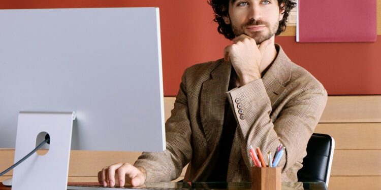 Man sitting at desk with computer, resting chin