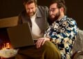 Two men looking at a laptop near a fireplace