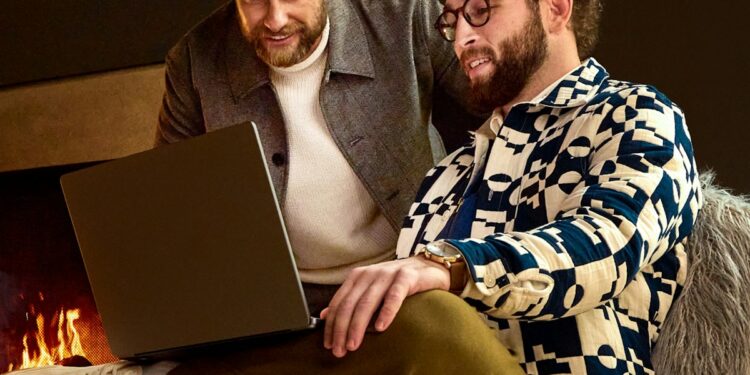 Two men looking at a laptop near a fireplace