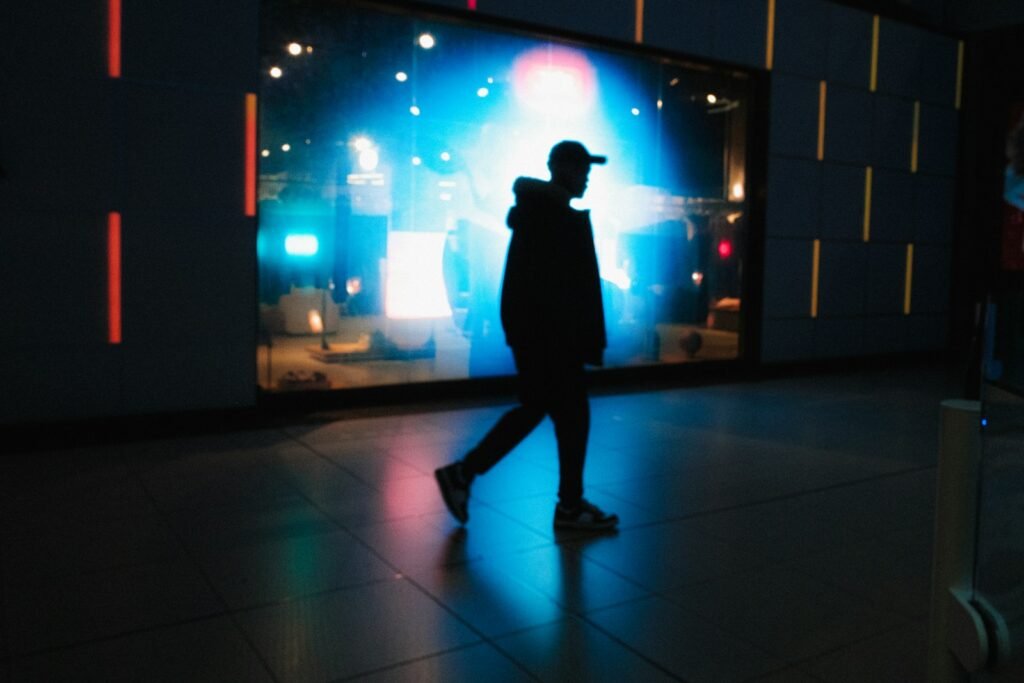 Silhouette of a man walking past a brightly lit display.