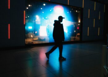 Silhouette of a man walking past a brightly lit display.