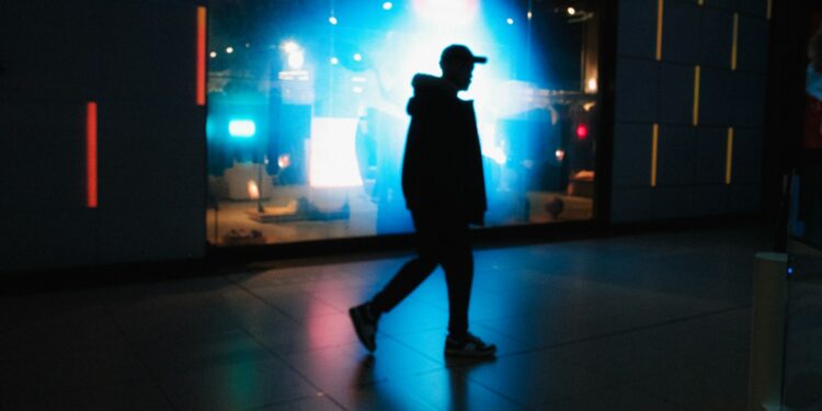 Silhouette of a man walking past a brightly lit display.